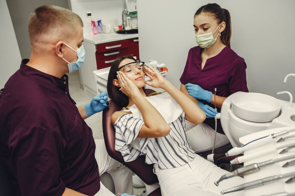 Patient wearing protective glasses during a dental exam while a dentist and assistant prepare for a routine checkup in a dental clinic.